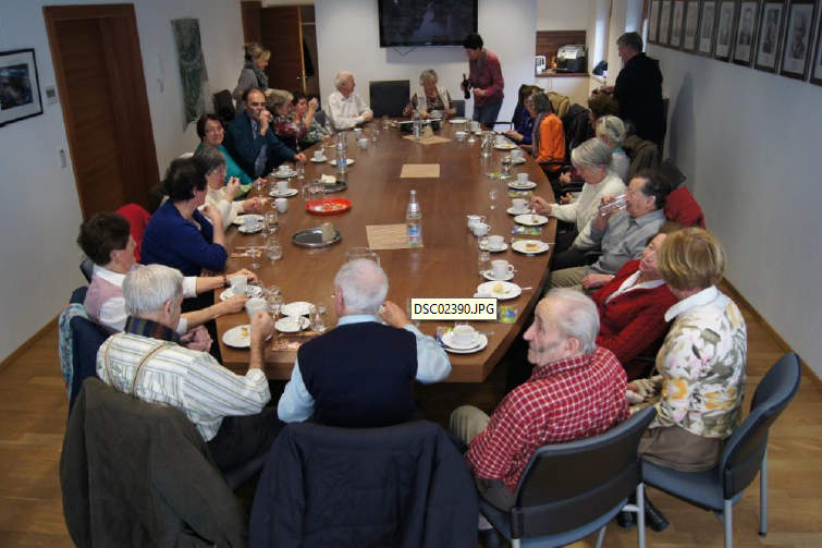 SeniorInnenrund um einen ovalen großen Tisch sitzen. Zirka 10-15 Personen.