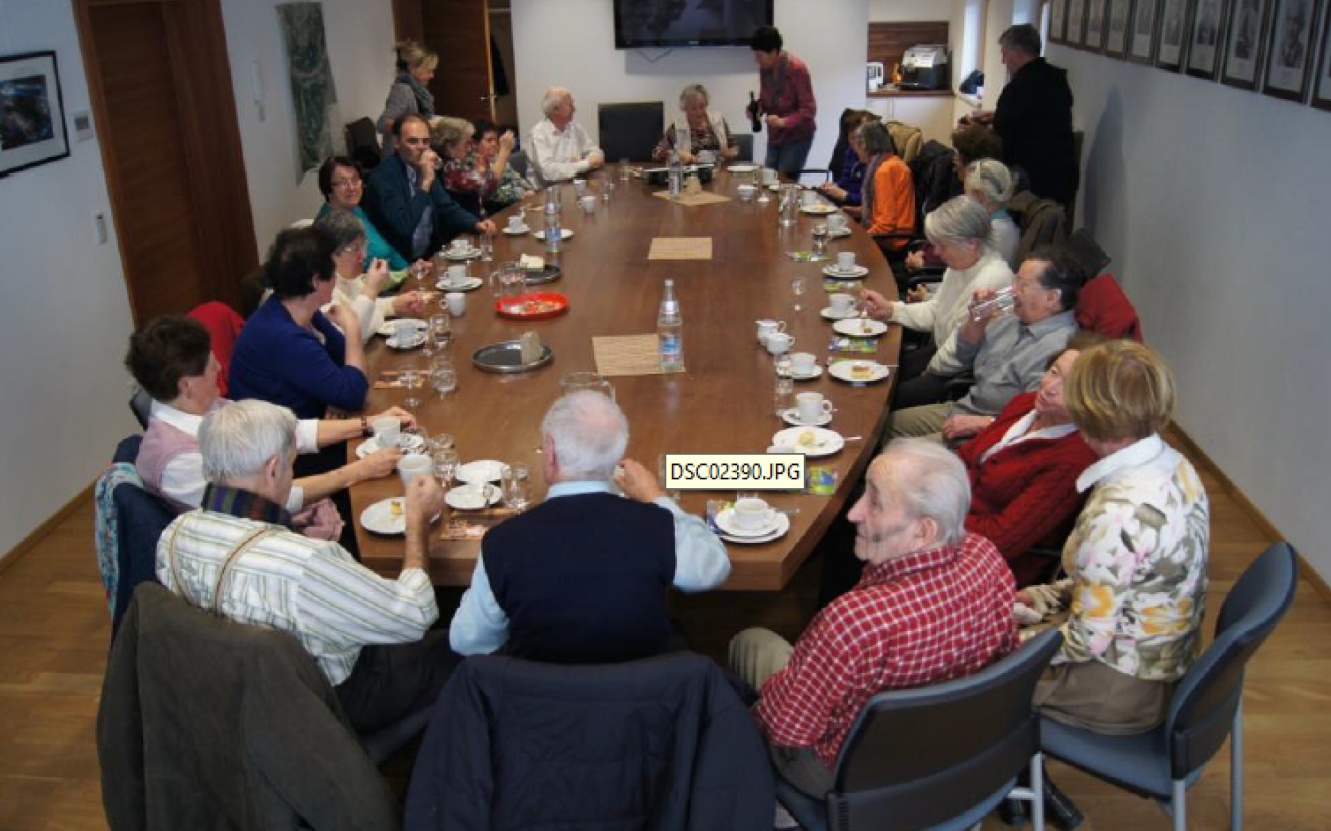 SeniorInnenrund um einen ovalen großen Tisch sitzen. Zirka 10-15 Personen.