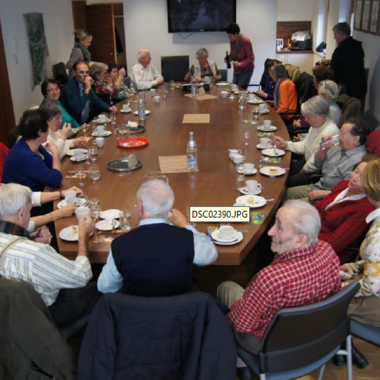 SeniorInnenrund um einen ovalen großen Tisch sitzen. Zirka 10-15 Personen.
